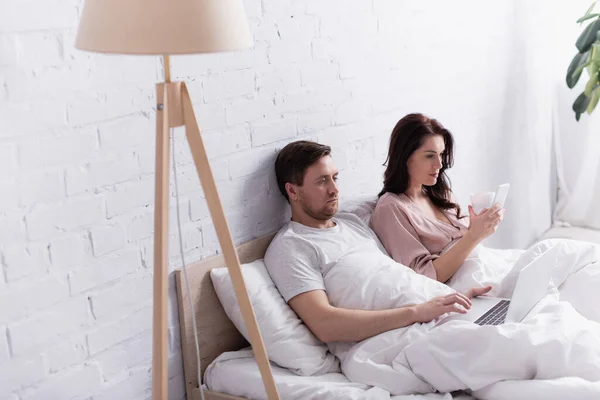 Man Met Laptop Buurt Van Vrouw Met Beker Smartphone Bed — Stockfoto