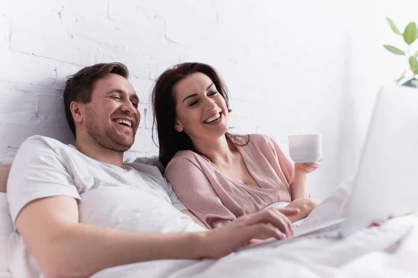 Smiling Man Using Laptop Blurred Foreground Wife Cup Bed — Stock Photo, Image