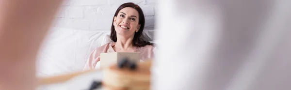 Mujer Sonriente Con Libro Mirando Marido Borroso Con Panqueques Dormitorio — Foto de Stock