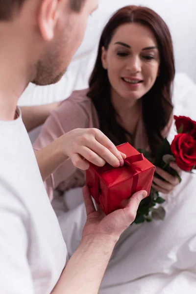 Чоловік Тримає Подарунок Біля Дружини Розмитими Ліжку Трояндами — стокове фото