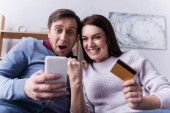 Vzrušený pár s kreditní kartou pomocí smartphone na rozmazané popředí 