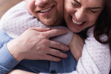 Cheerful woman in sweater hugging bearded husband  clipart