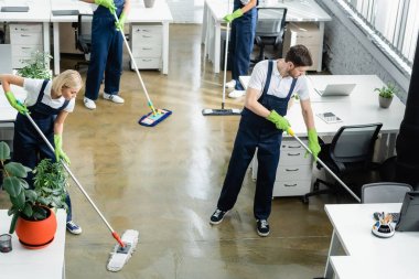 High angle view of cleaners washing floor near tables in office  clipart