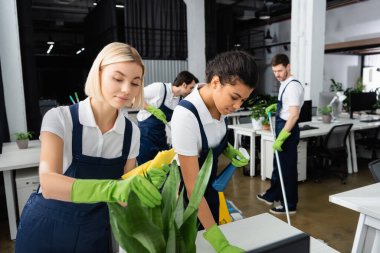 Çok ırklı temizlikçiler ofiste fabrika ve masa temizliyor. 