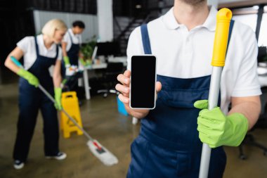 Cleaner holding smartphone and mop in office  clipart