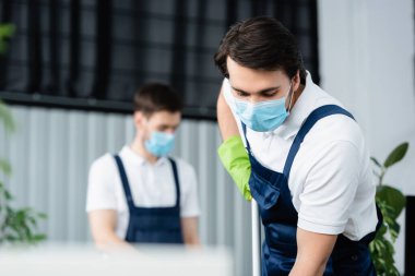 Sağlık maskeli temizlik şirketinin çalışanı ofisinde paspas tutuyor. 