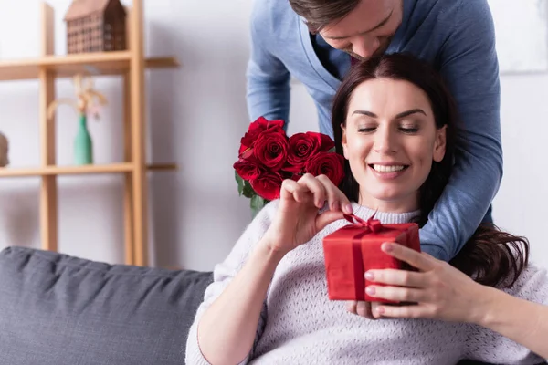 Mulher Sorridente Segurando Presente Com Arco Perto Marido Com Rosas — Fotografia de Stock