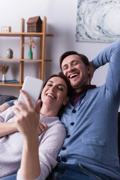 Fröhlicher Mann Sitzt Neben Frau Mit Handy Verschwommenen Vordergrund — Stockfoto