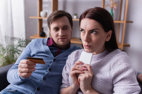 Bulanık Kocanın Yanında Kredi Kartıyla Cep Telefonu Tutan Düşünceli Kadın — Stok fotoğraf