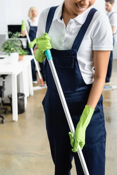 Smiling African American Cleaner Holding Mop Colleagues Blurred Background Office — Stock Photo, Image