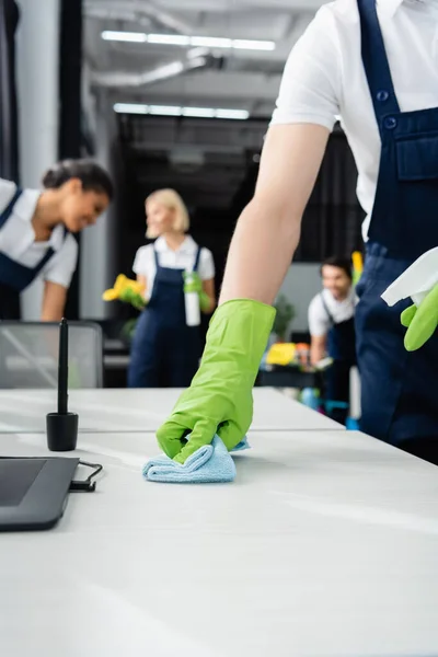 Worker of cleaning company washing table with detergent near graphic tablet on table