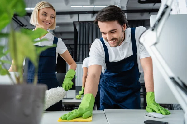 Sonriente Trabajador Servicio Limpieza Mesa Limpieza Cerca Computadora Colega Oficina —  Fotos de Stock