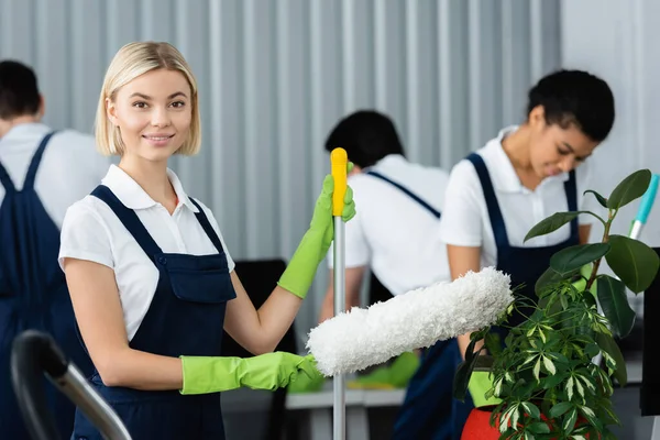 Smiling Cleaner Mop Dust Brush Looking Camera Plants Office — Stock Photo, Image