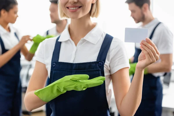 Limpiador Sonriente Apuntando Tarjeta Vacía Cerca Colegas Borrosos Oficina — Foto de Stock