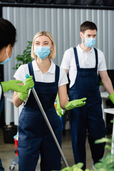 Interracial cleaners in medical masks and uniform standing in office 