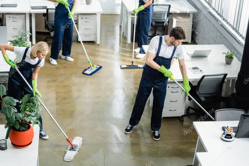 High angle view of cleaners washing floor near tables in office 