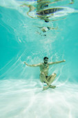 Muslimische Schwimmerin in Schutzbrille schwimmt am Grund des Beckens 