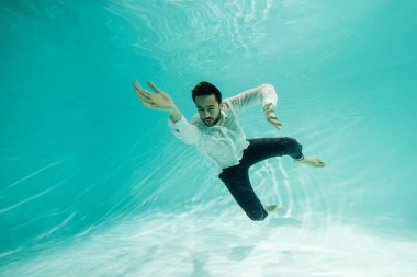 Genç Müslüman iş adamı gözleri kapalı havuzda suyun altında yüzüyor. 