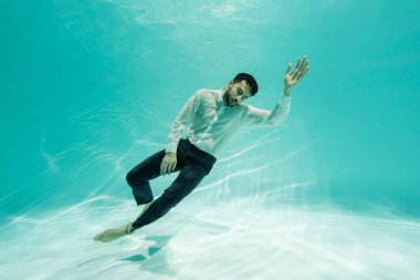 Arabian businessman in formal wear swimming near bottom of pool  clipart