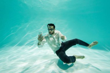 Gözlüklü Arap işadamı yüzme havuzunda cep telefonuna bakıyor. 