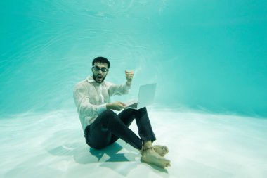 Heyecanlı Müslüman iş adamı evet işareti yapıyor ve elinde dizüstü bilgisayarla havuzda. 