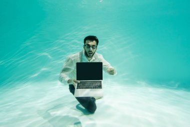 Şaşırmış Arap işadamı yüzme havuzunda boş ekranla dizüstü bilgisayarı işaret ediyor. 