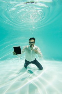 Gülümseyen Arap yönetici suyun altındaki dijital tableti işaret ediyor 