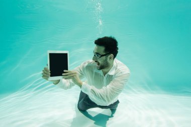 Yüzme havuzunda boş ekranlı dijital tablet tutan neşeli Müslüman iş adamı 