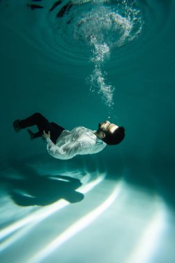 Arabian man in formal wear swimming near bubbles of air underwater  clipart