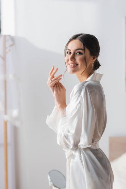 Beyaz cüppeli mutlu gelin yatak odasında kameraya gülümsüyor.