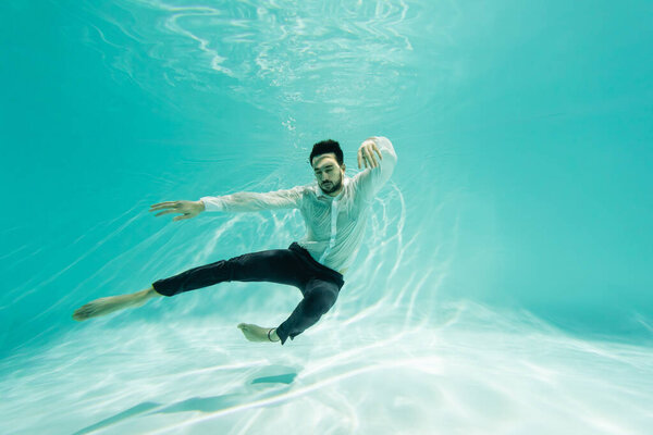 Young arabian businessman in formal wear swimming in pool with closed eyes 