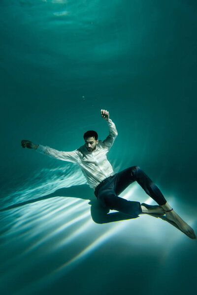 Arabian man in formal wear sitting on bottom of swimming pool 