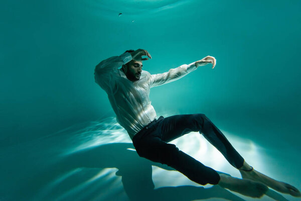 Arabian businessman with closed eyes swimming underwater in pool 