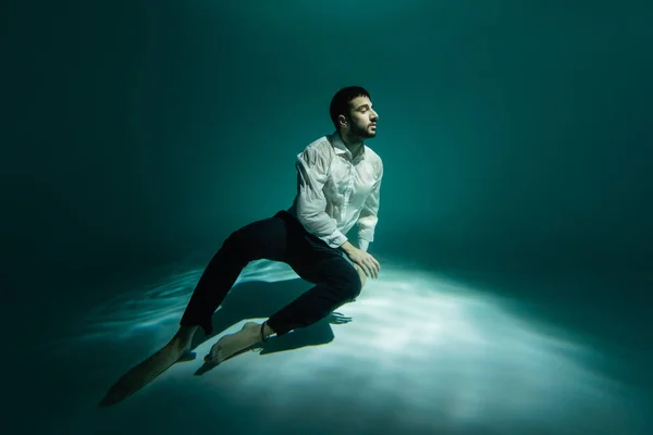 Arabian man in shirt and pants swimming near bottom of pool