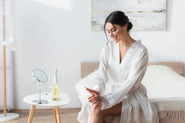 Lächelnde Braut Satinmantel Neben Spiegel Und Champagner Auf Nachttisch — Stockfoto