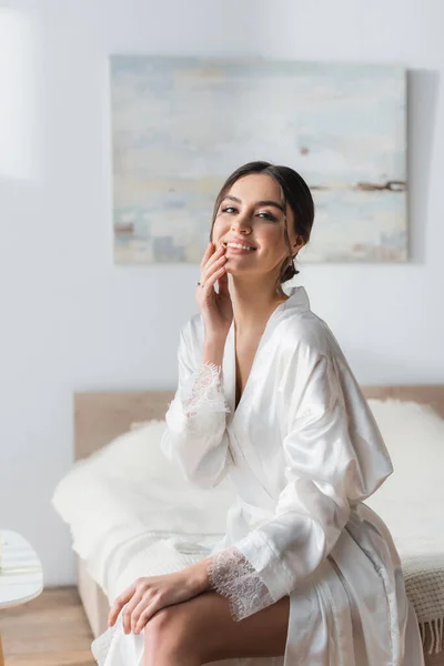 Brunette Bride Silk Robe Smiling Camera While Touching Face Bedroom — Stock Photo, Image