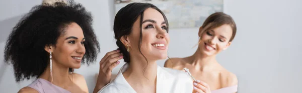 Happy Bride Looking Away While Interracial Bridesmaids Doing Hairstyle Banner — Stock Photo, Image