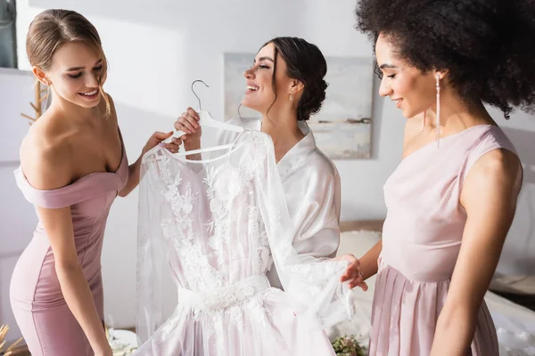 Madrinhas Inter Raciais Segurando Vestido Casamento Branco Perto Mulher Alegre — Fotografia de Stock