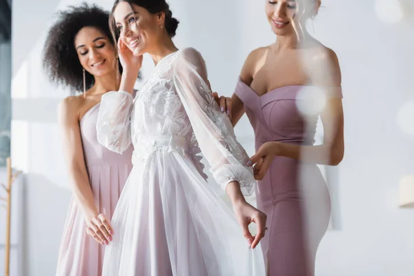 幸せな女性のウェディングドレスを調整する多文化の花嫁介添人 ぼやけた前景 — ストック写真