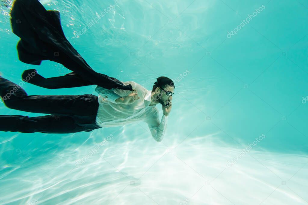 Muslim businessman holding jacket and talking on smartphone underwater 