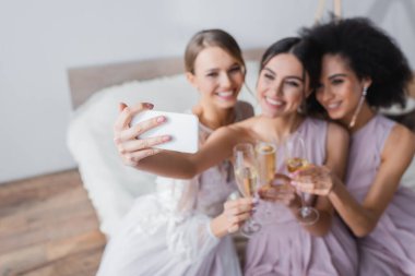 Neşeli kadın, bulanık arka planda gelinle ve Afrikalı Amerikalı arkadaşıyla selfie çekiyor.