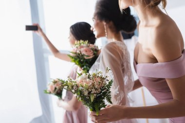 Gelin ırklar arası nedimelerle selfie çekiyor düğün buketleri tutuyor, geçmişi bulanık.