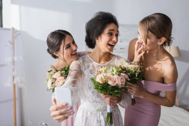 Gülen Afrikalı Amerikalı gelin neşeli arkadaşlarıyla selfie çekiyor, bulanık ön plan
