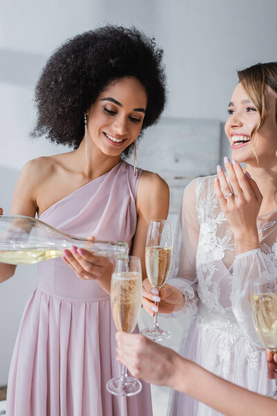 elegant african american woman pouring champagne near happy bride