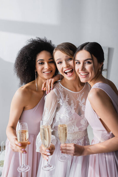 excited bride with friends smiling at camera while holding champagne glasses