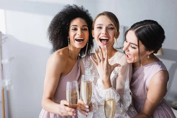 兴奋的女人带着香槟酒杯在跨种族伴娘身边展示结婚戒指 — 图库照片