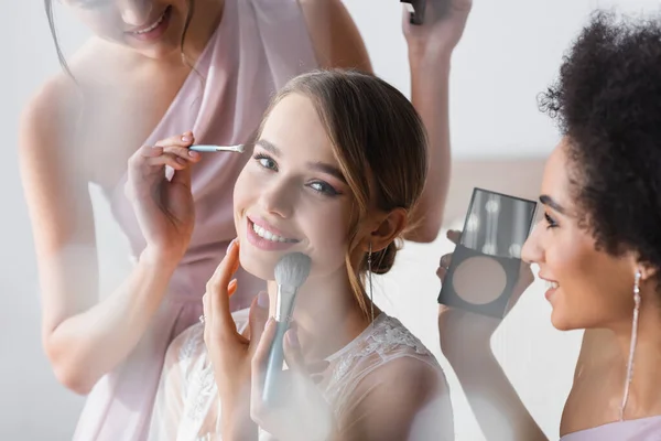 Pretty Bride Smiling Camera While Interracial Women Applying Makeup Blurred — Stock Photo, Image