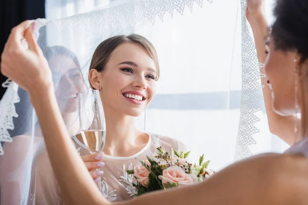 アフリカ系アメリカ人花嫁介添人シャンパングラスと花束で幸せな花嫁のベールを保持 — ストック写真