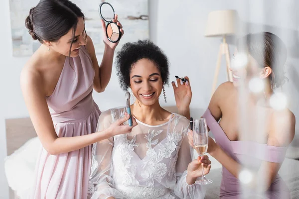 快乐的非洲裔美国新娘举着香槟酒杯 而朋友们则在化妆 前景暗淡 — 图库照片