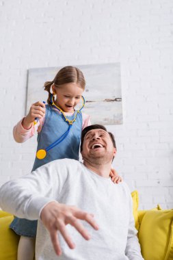 Baba doktorculuk oynarken kızının oyuncak şırıngasını tutarken korkmuş numarası yapıyor.